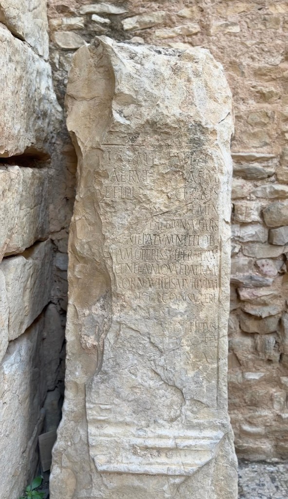 Ancient stone monument with inscriptions in Bulla Regia, partially surrounded by brick walls.