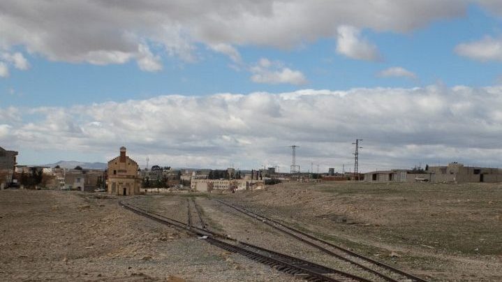 A set of railroad tracks extending into the distance across a barren landscape with scattered buildings in Haïdra, Tunisia
