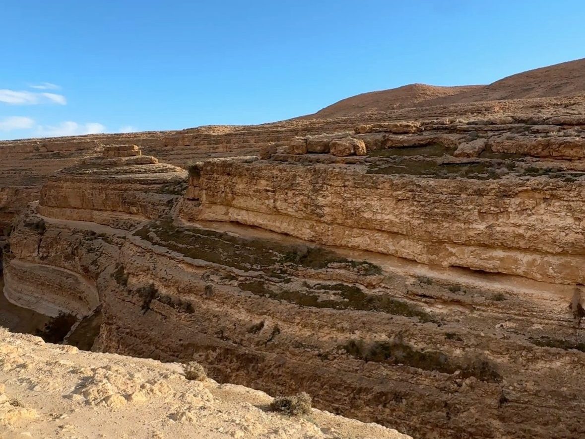 Panoramic view of layered rocky cliffs under a clear blue sky at Mides Canyon, Tunisia.