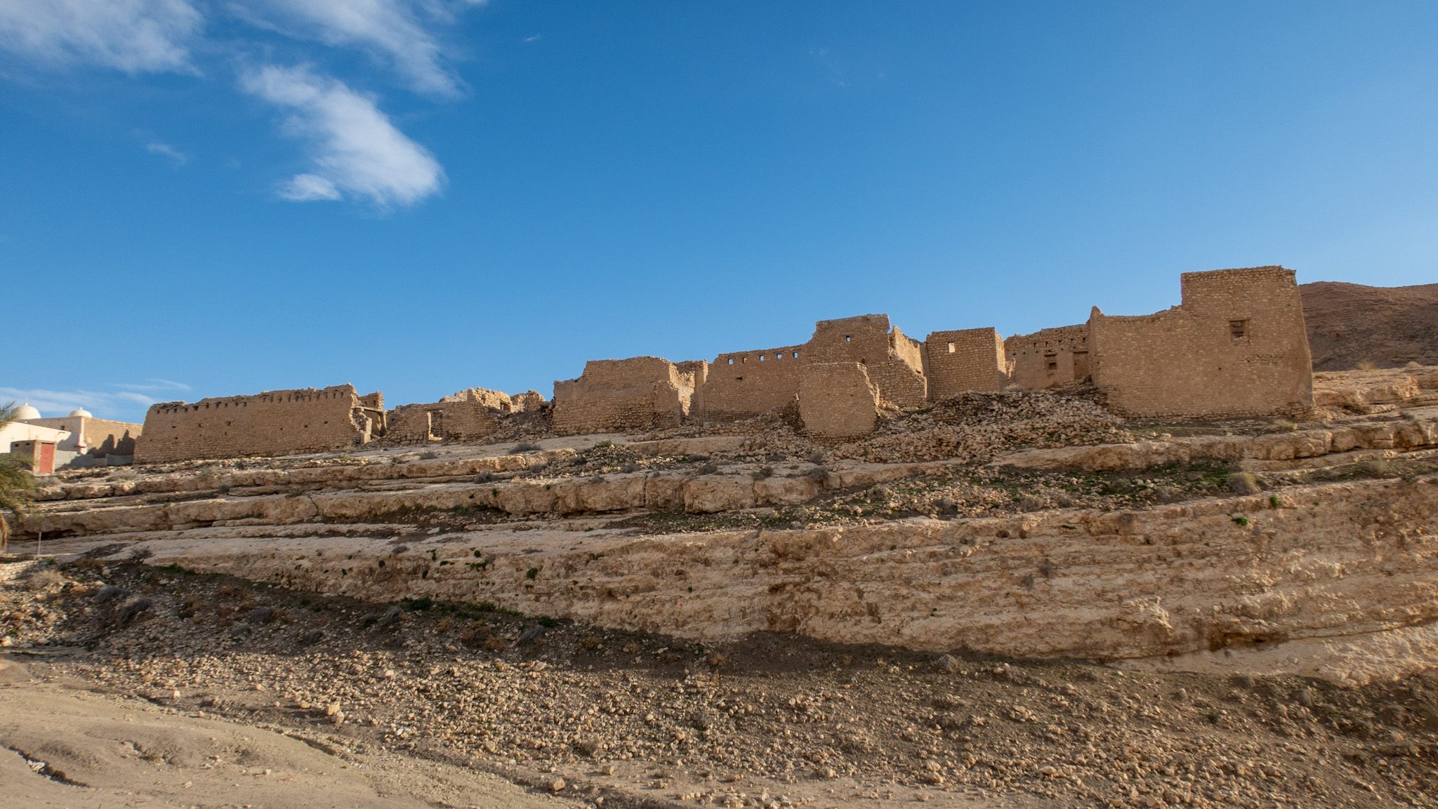 Ruins of ancient buildings within an ancient village in Mides Canyon, Tunisia on a hillside under a blue sky.